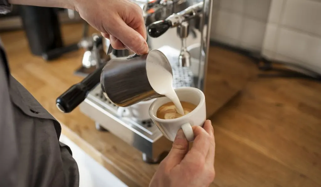 barrista pouring milk to cappuccino