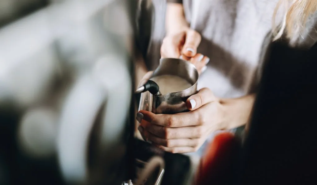 woman frothing milk in a coffee shop