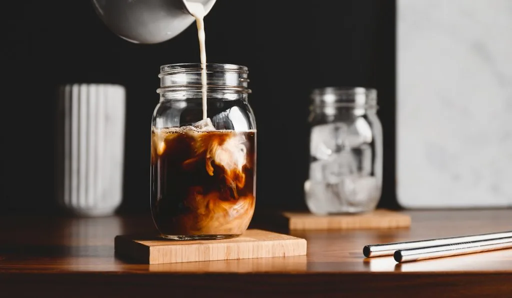 pouring milk into a glass of coffee